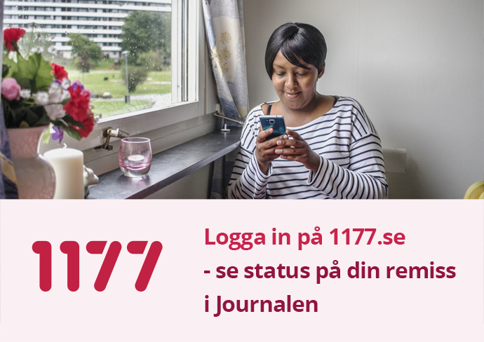 Ung kvinna sitter vid köksbordet och tittar i mobiltelefonen