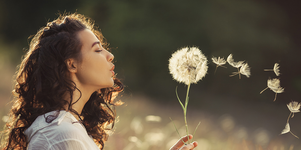 Kvinna blåser på maskrosboll som om det vore rökpuffar