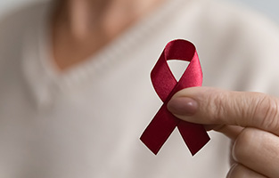 Bild på en hand som håller i  symbolen för aids - ett rött band format som en ögla