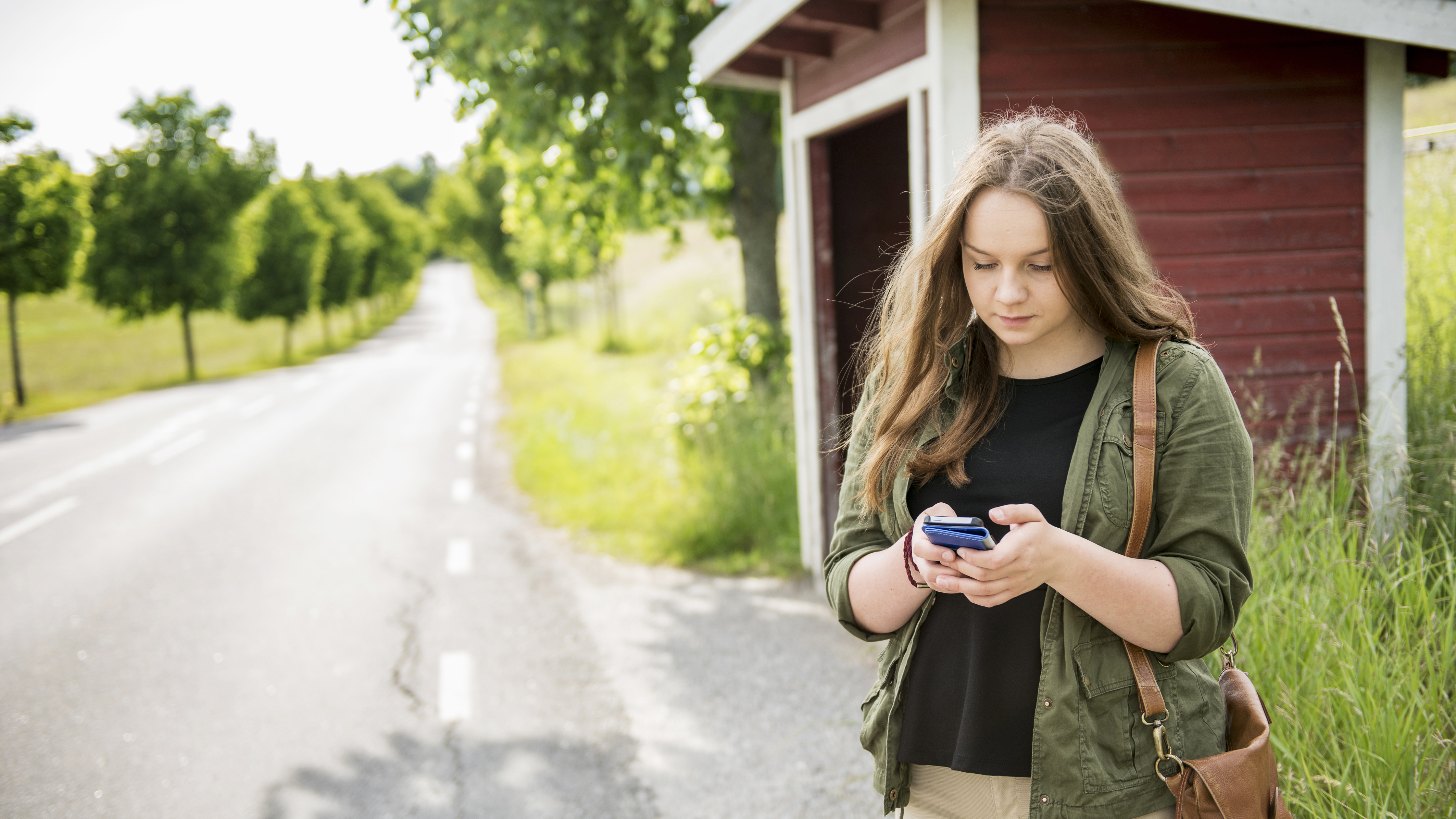 Ung kvinna står utomhus och chattar med 1177 direkt via sin mobiltelefon 