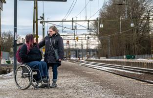 Två personer på en perrong. En person sitter i rullstol och en står bredvid.