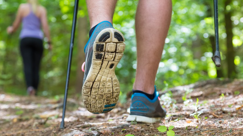 Närbild från knäna och nedåt på person som går stavgång med sneakers i skogen